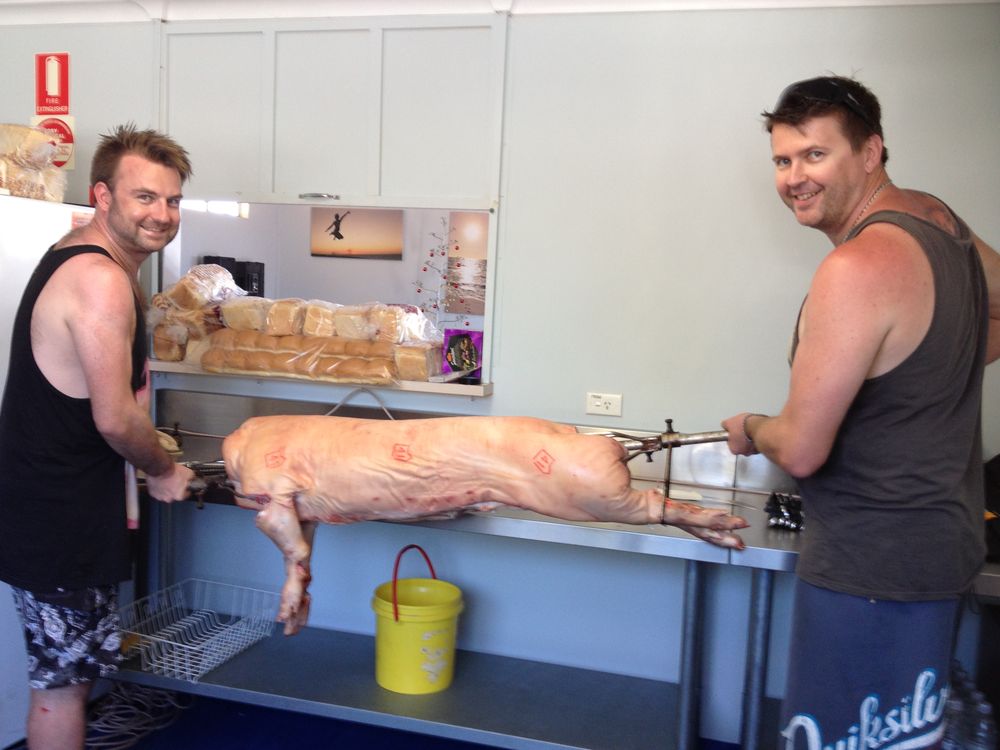 Volunteers loading a whole pig onto the spit in the John Batten Hall kitchen